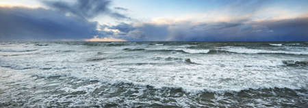 Baltic sea shore at sunset. Dramatic storm clouds, crashing waves. Panoramic seascape. Liepaja,...