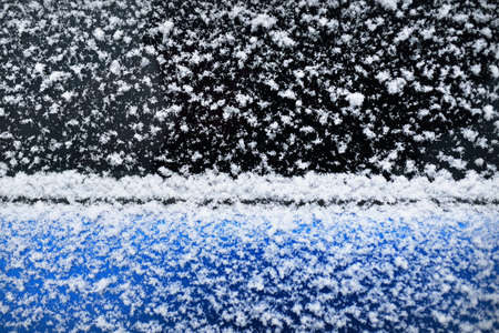Snowflakes on a car window after a blizzard, close-up. Cold weather, winter, climate change, cleaning and care, dangerous driving conceptsの写真素材