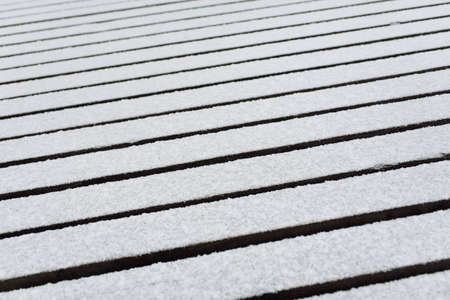 Snow-covered modern wooden pier (jetty, boardwalk) over the frozen river. Ice, frost, snow textures. Decoration, design, graphic resources, copy space, winter backgroundの写真素材