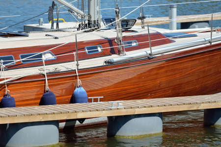 Elegant modern sailing boat with wooden teak deck moored to a pier in a yacht marina. Nautical...