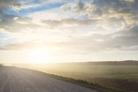 Empty country road through the field after the storm. A view from the car. Idyllic rural scene. Colorful glowing sunset clouds. Transportation, road trip, freedom, wanderlust, remote places conceptsの写真素材