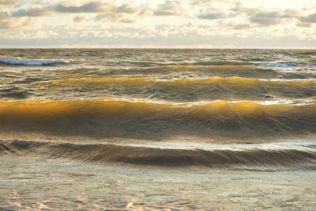 Baltic sea shore after the storm. Sunset, soft golden sunlight. Water surface texture, crashing waves and splashes. Picturesque panoramic scenery, background. Nature, environment, ecology conceptsの写真素材