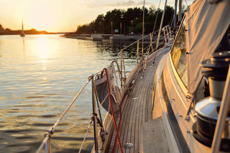 Old classic sailboat with wooden teak deck moored to a pier in a yacht marina at sunset. Vacations,...