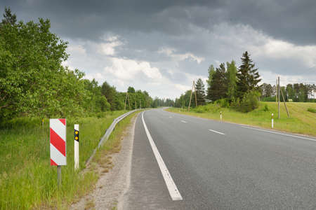An empty highway (new asphalt road) through the field and forest on a summer day. Dramatic storm...
