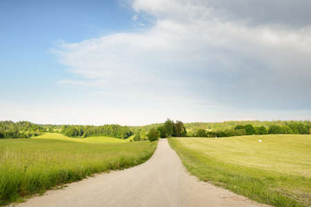 An empty rural road through the field and forest at sunset. Glowing sky after the rain. Tourism,...