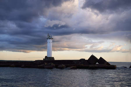 Lighthouse with a solar battery. Baltic sea. Dramatic sunset sky after the storm. Glowing clouds, golden sunlight. Symbol of hope and peace. Architecture, travel destinations, navigation, sailingの写真素材