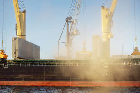Large cargo ship (bulk carrier, 179 meters length) with cranes loading in the port terminal. Baltic sea. Freight transportation, logistics, global communications, economy, business, industry, supplyの写真素材