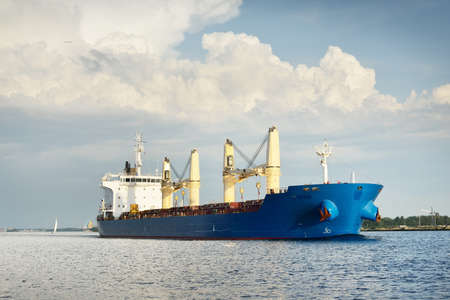 Large cargo ship with cranes leaves the port at sunset. Baltic sea. Dramatic storm sky. Freight...