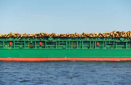 Large green cargo ship, 100 meters length, with firewood sailing in the Baltic sea. Freight transportation, business, ecological problem, deforestation, lumber industry, politics, corruption conceptsの写真素材