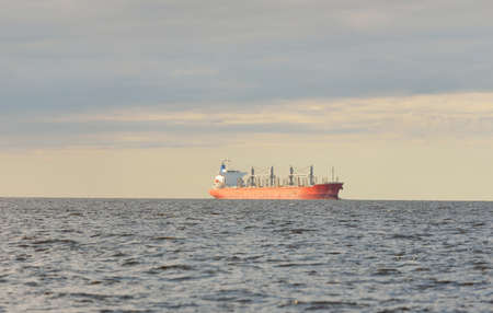 Large red bulk carrier (179 meters length) sailing in an open Baltic sea. Dramatic sky. Freight transportation, nautical vessel, logistics, global communications, economy, business, industryの写真素材
