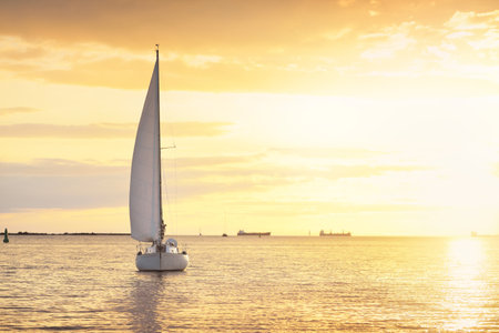 Sloop rigged yacht sailing in the Baltic sea. Sunset. Dramatic sky after the storm, golden sunlight. Transportation, travel, cruise, yachts racing, sport, recreation, leisure activity, lifestyleの写真素材