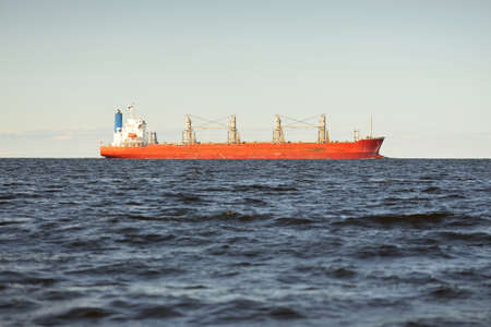 Large red bulk carrier (179 meters length) sailing in an open Baltic sea. Dramatic sky. Freight transportation, nautical vessel, logistics, global communications, economy, business, industryの写真素材