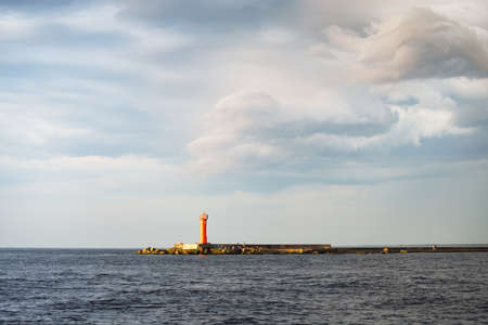 Baltic sea after the storm, panoramic view from a sailing boat. Lighthouse. Dramatic sunset sky. Glowing clouds, golden sunlight. Idyllic seascape. Nature, cruise, travel destinationsの写真素材