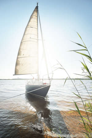 Blue sloop rigged yacht anchored to the sandy shore (beach). Sailing in Sweden, Europe. Nature, summer vacations, recreation, cruise, sport, transportation, private vessel for rentの写真素材
