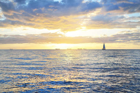 Dramatic sunset sky above the sea. Colorful glowing golden clouds, still water surface texture close-up. Sailing after the storm, view from the yacht. Epic seascape. Nature, fickle weatherの写真素材