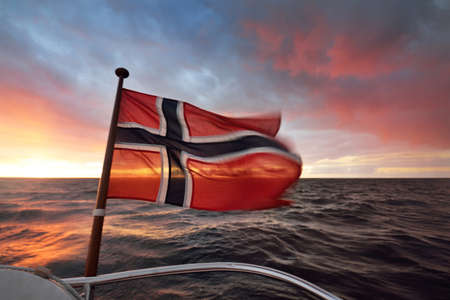 Flag of Norway on the private vessel (yacht) against colorful cloudy sunset sky, close-up. Baltic sea. Travel destinations, national identity, symbolism, patriotism. Motion blurの写真素材