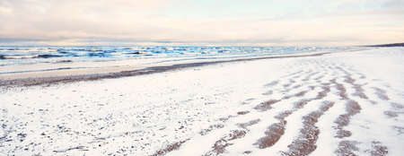 A view from the snow-covered Baltic sea shore at sunset. Riga bay, Latvia. Colorful dramatic cloudscape. Fickle weather, waves and water splashes. Winter tourism, global warming themeの写真素材