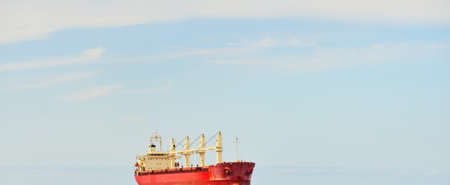 Large red bulk carrier (cargo ship) with a cranes sailing in an open sea from Europoort. Clear blue sky with cirrus clouds. Rotterdam, Netherlands. Global communications, logistics, industry themeの写真素材