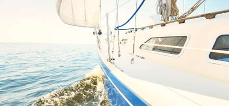 White yacht sailing on a sunny summer day. Close-up view from the deck to the bow and sails. Waves and water splashes. Clear blue sky. Baltic sea, Swedenの写真素材