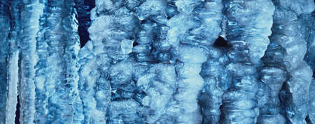 Large blue icicles close-up, cliff in the background. Frozen water, ice texture. Abstract art,...