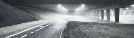 Concrete bridge above the empty illuminated motorway, bicycle road and pedestrian walkway at night....