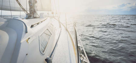 White yacht sailing in an open sea at sunset. Close-up view from the deck to the bow and sails....