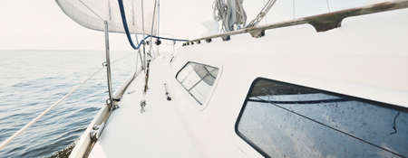 White yacht sailing on a sunny summer day. Close-up view from the deck to the bow and sails. Waves...