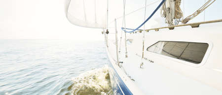 White yacht sailing on a sunny summer day. Close-up view from the deck to the bow and sails. Waves and water splashes. Clear blue sky. Baltic sea, Swedenの写真素材