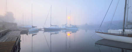 Sailing boats moored to a pier in a thick white morning fog at sunrise, close-up. Yacht club in Kiel, Germany. Sport, recreation, transportation themeの写真素材