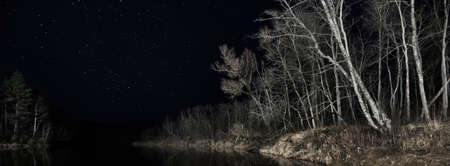 Epic starry sky above the forest lake in autumn. Birch and coniferous tree silhouettes in the dark, Gauja national park, Sigulda, Latvia. Reflections in the crystal clear water. Mystic landscapeの写真素材
