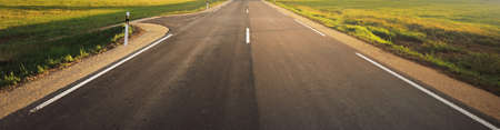 An empty highway (new asphalt road) through the green country fields at sunset. Travel destinations,...