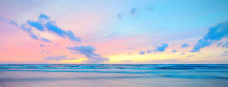 Baltic sea at sunset. Dramatic twilight sky, blue and pink glowing clouds, golden sunlight. Waves, splashing water. Picturesque scenery, seascape, cloudscape, nature. Panoramic view, long exposureの写真素材