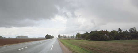 Empty highway (asphalt road) through the fields. Dramatic sky before the rain and thunderstorm. Concept landscape. Rural scene. Darkness, fall season, fickle weather, dangerous driving, road tripの写真素材