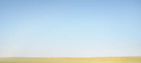 Green plowed country field in a morning fog at sunrise. Clear blue sky. Idyllic rural scene. Agriculture, environmental conservation, ecology, natureの写真素材