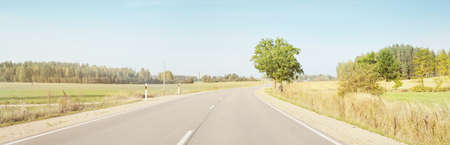 Country asphalt road (highway) through the field and forest on a clear day. Warm midday sunlight, clear sky. A view from the car. Travel destinations, vacations, freedom, driving, transportationの写真素材
