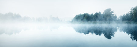 Picturesque scenery of the forest lake in a thick white fog. Reflections on the water. Dark atmospheric landscape. Fall season. Nature, ecology, environmental conservation, eco tourismの写真素材