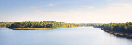 Panoramic aerial view of the forest and a blue river. Clear sky, pure warm morning sunlight. Colorful golden trees close-up. Early autumn in Latvia. Idyllic rural sceneの写真素材