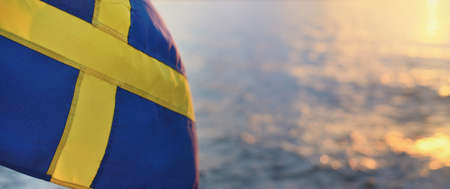 Flag of Sweden on a private vessel (yacht). Golden sunset clouds blurred in bokeh. Sailing in MÃ¤laren lake. Patriotism, national identity, symbol, independence, politicsの写真素材