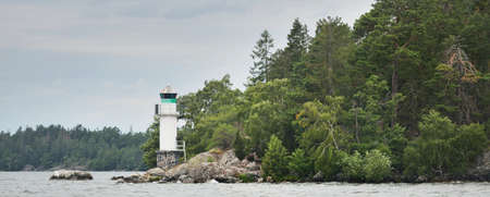 Sailing in MÃ¤laren lake, Sweden. Rocky shore, forest. Small white lighthouse. Nature, environment, travel destinations, ecotourism, hiking, vacations, architecture, navigationの写真素材