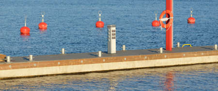 Orange mooring buoys and lifebuoys in the new yacht harbor (marina), close-up. Water surface texture. A view from the pier. Work safety, special equipment, sailing, cruise, sport, recreation. Latviaの写真素材