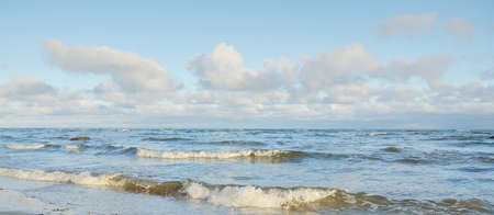 Panoramic view of the Baltic sea in winter. Clear blue sky with glowing cumulus clouds. Water surface texture, waves and water splashes close-up. Fickle weather, climate change, nature, seascapeの写真素材