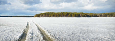 Frozen lake and pine forest at sunset. Ice texture. Tractor tracks close-up. Dramatic blue sky, cloudscape. Winter wonderland. Nature, ecology, climate change, ecotourism, fickle weatherの写真素材