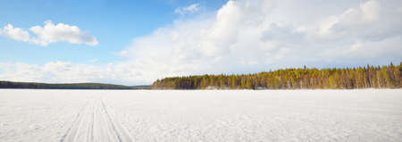Frozen lake and pine forest at sunset. Ice texture. Tractor tracks close-up. Dramatic blue sky, cloudscape. Winter wonderland. Nature, ecology, climate change, ecotourism, fickle weatherの写真素材