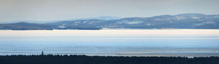 Panoramic aerial view of the lake shores, forest and mountain peaks. Winter landscape. Epic sunset sky. Environment, climate change, ecology, ecotourism, remote placesの写真素材