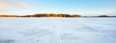 Frozen lake and snow-covered pine forest at sunset. Ice texture. Dramatic sky, soft sunlight. Idyllic winter scene. Nature, environmental conservation, ecology, climate change, ecotourism, Christmasの写真素材
