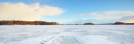 Frozen lake and snow-covered pine forest at sunset. Ice texture. Dramatic sky, soft sunlight. Idyllic winter scene. Nature, environmental conservation, ecology, climate change, ecotourism, Christmasの写真素材