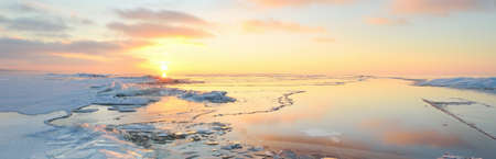 Snow-covered shore of the frozen lake at sunset. Stunning pink cloudscape. Symmetry reflections on the water. Winter wonderland. Finlandの写真素材