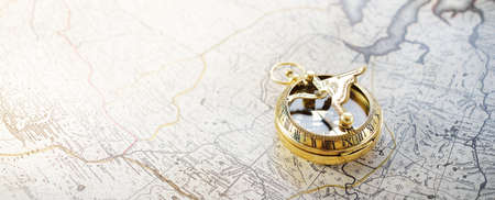 Retro styled golden compass (sundial) and old white nautical chart close-up. Vintage still life. Sailing accessories. Travel and navigation themeの写真素材