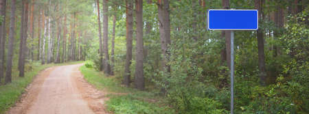 A dirt road through the evergreen summer forest on a clear day. Street sign close-up. Environmental...
