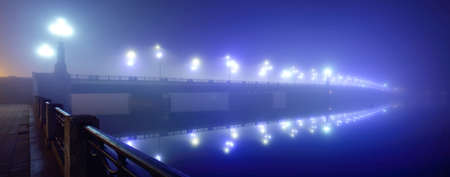 Illuminated empty Stone bridge in a fog at night. Lanterns close-up. Symmetry reflections on the...